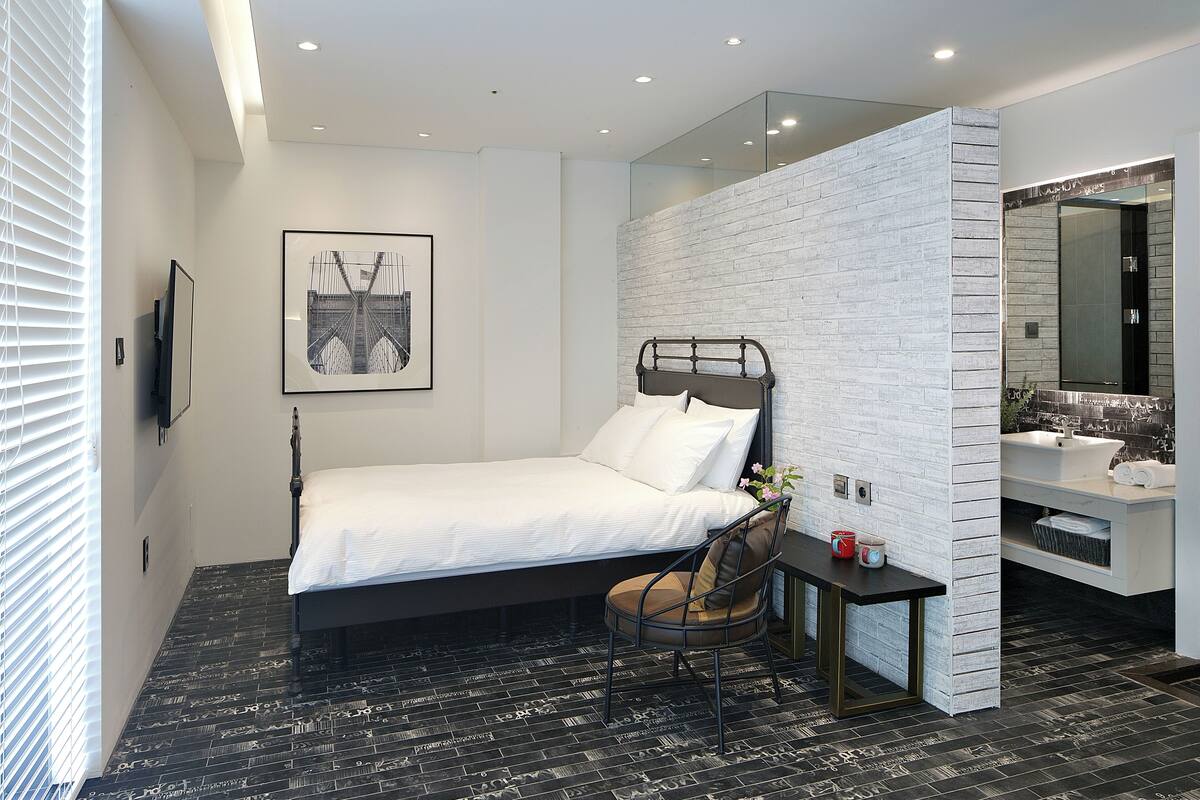 A modern bedroom with a bed, a desk, and a bathroom with a mirror and sink.