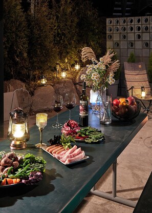 Un espace de restauration en plein air avec une variété de plats et de boissons, notamment une bouteille de vin, une lanterne et un panier de fruits.