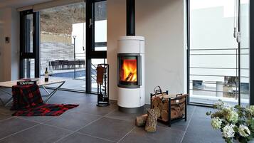 A modern living room with a wood-burning stove, a dining area with a table and chairs, and a large window offering a view of the outdoors.