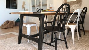Een eethoek met een houten tafel, zwart-witte stoelen, een glazen kast en een geweven spiegel aan de muur.