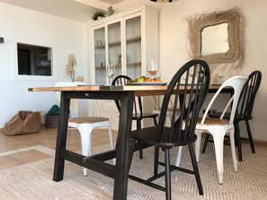 A dining area with a wooden table, black and white chairs, a glass cabinet, and a woven mirror on the wall. - La Petite Foret Sea-view Apartment in Mascarat (Altea)