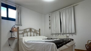 Een slaapkamer met een bed, een bedlamp, een raam met gordijnen en een radiator.