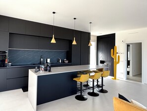 A modern kitchen with a central island, bar stools, pendant lighting, and a cactus decoration. - Villa Nanni, Contemporary, Pool and Garden (Sicilia)