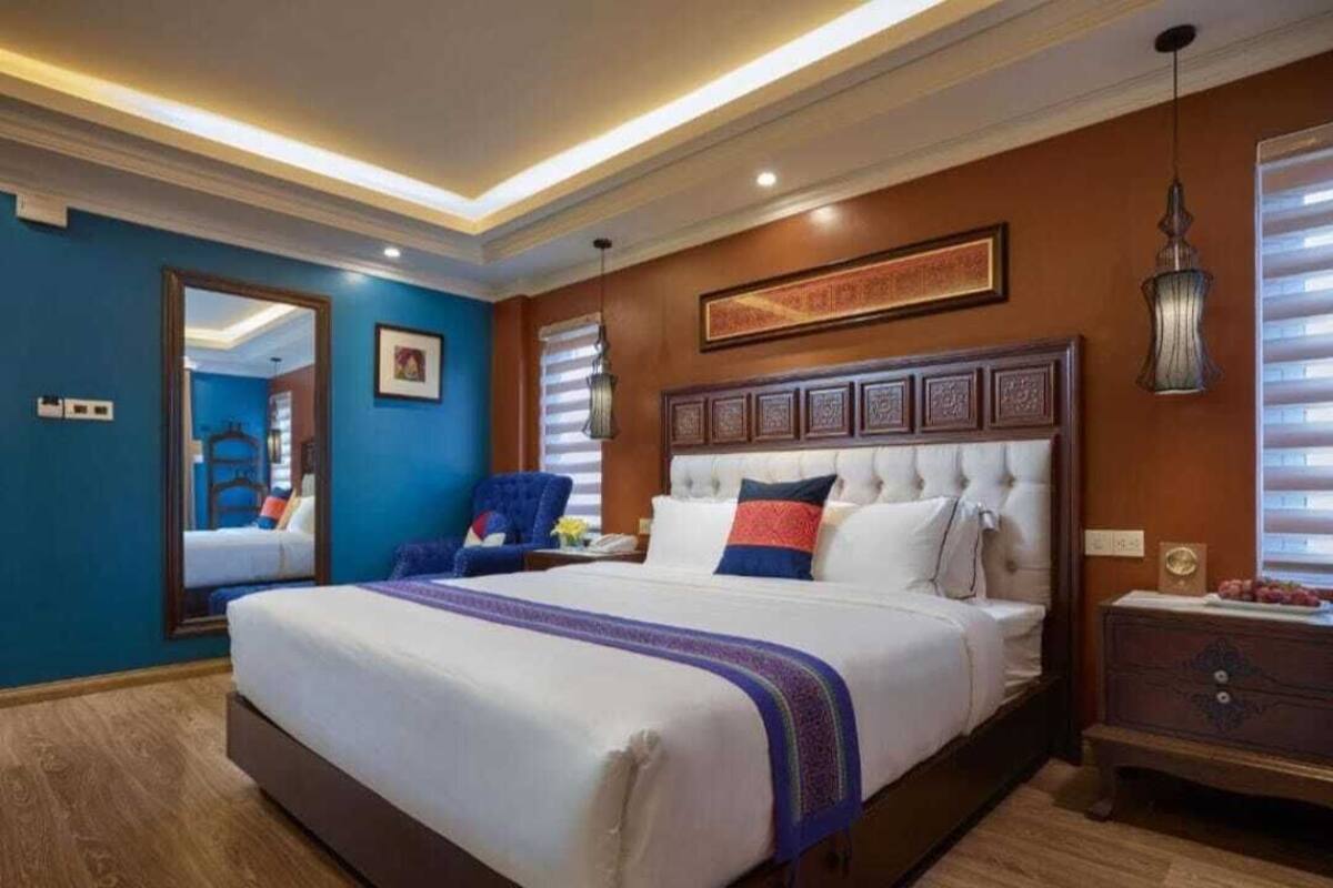 Ein Hotelzimmer mit einem großen Bett, einer Holzkommode, einem blauen Sessel und einem gerahmten Kunstwerk über dem Bett.