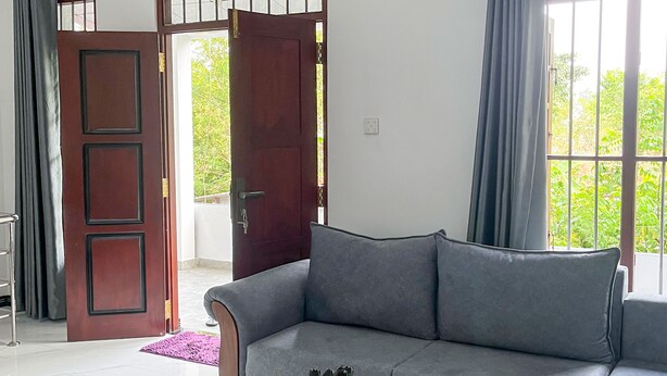 A modern living room with a grey sofa, a glass coffee table, and a wooden door. - Rivora 2-Bedroom Apartment in Aluthgama Near Bentota Beach (Aluthgama)