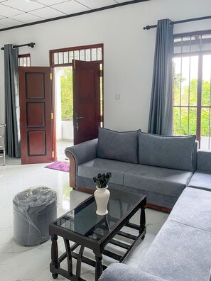 A modern living room with a grey sofa, a glass coffee table, and a wooden door.