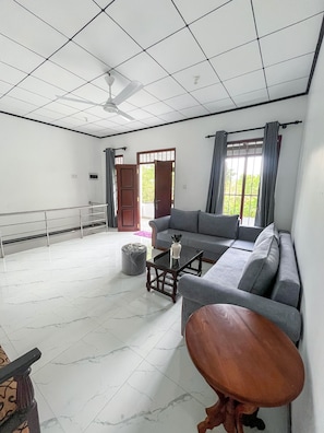 A spacious room with a large grey sofa, a small wooden table, and a ceiling fan.