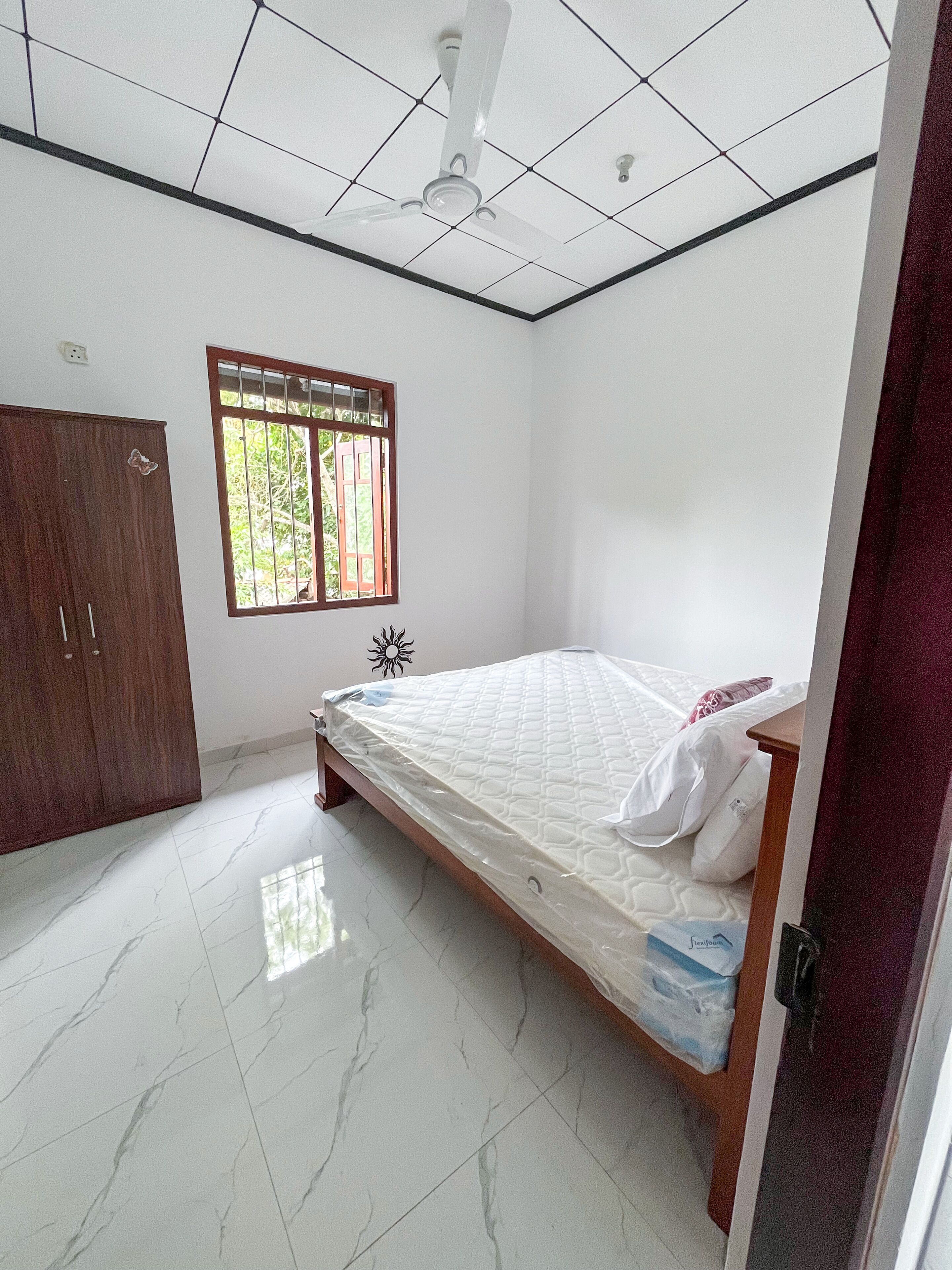 A bedroom with a bed, a wardrobe, a window, and a ceiling fan.