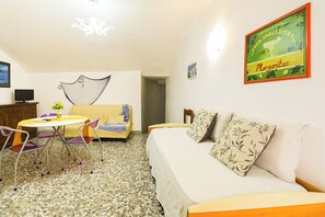 Une pièce comprenant un lit, un canapé, une table à manger avec des chaises, un téléviseur et un mur orné d’une affiche.