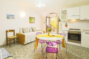 Un espace de vie compact comprenant un coin cuisine, un coin repas avec une table et des chaises, un canapé et une petite fenêtre.