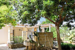 A stone water fountain, a cactus, and a building with a tiled roof and a door. - La Beccaccia by Casa di Marco (La Corte)