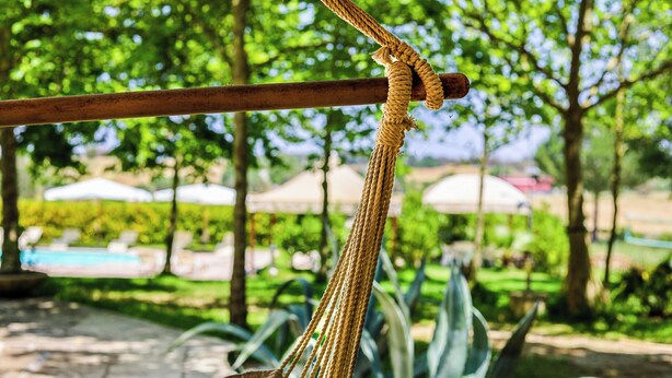 A rope tied around a wooden pole in an outdoor setting with greenery and umbrellas in the background. - Maria nel Casale Mastria by Casa di Marco (Neviano)