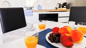 Een ontbijttafel met fruit, sinaasappelsap, een koffiezetapparaat en een waterkoker in een moderne keuken.