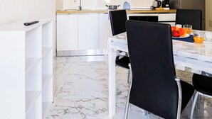 Een moderne keuken met witte kastjes, een marmeren vloer en een eethoek met een tafel en stoelen.