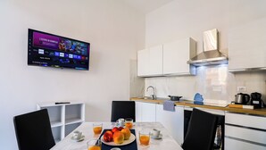 Een moderne keuken met een ontbijttafel, een televisiescherm waarop een programma draait, en een schoon, minimalistisch design.