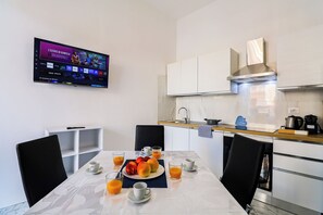 Una cocina moderna con una mesa de desayuno dispuesta, un televisor mostrando un programa y un diseño limpio y minimalista.