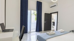 Una moderna camera d'albergo con un letto, una scrivania con un portatile, un angolo doccia e vista sull'esterno.