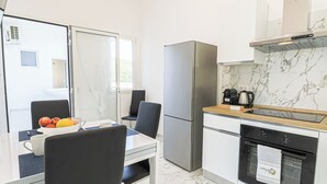 Una cucina moderna con frigorifero, forno e macchina del caffè. C'è un tavolo da pranzo con sedie e una ciotola di frutta.