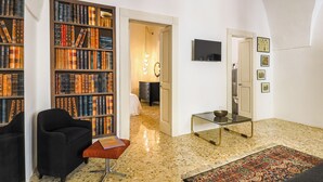 A spacious living room with a large bookshelf, a comfortable armchair, a glass coffee table, and a patterned rug. - Palazzo Frascà by Casa di Marco (Parabita)