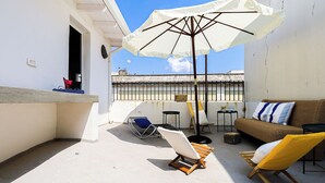 A rooftop terrace with a white umbrella, a wicker sofa, a yellow chair, and a blue lounge chair. - Palazzo Frascà by Casa di Marco (Parabita)