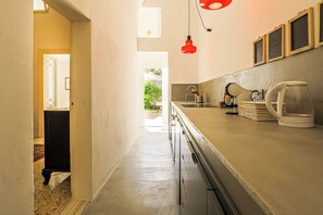 Un pasillo estrecho con una zona de cocina a la derecha, que incluye una cafetera, un hervidor y un lavabo.