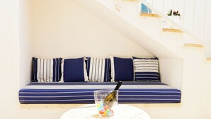 En hyggelig siddekrog med en stribet sofa og puder, et glastilbord med en flaske og farverige genstande, samt en trappe med en pynteting.