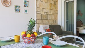 Ein Essbereich mit einem für zwei gedeckten Tisch, mit einer Ananas und verschiedenen Früchten, einer Obstschale sowie bunten Tassen und Tellern.