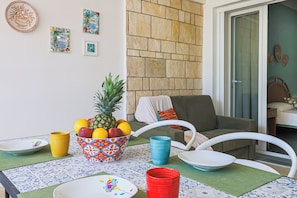 A dining area with a table set for two, featuring a pineapple and assorted fruits, a bowl of fruit, and various colored cups and plates. - Tamarè by Casa di Marco (Conchiglie-Alto Lido)