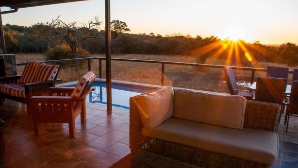 A terrace with wicker furniture, a pool, and a view of the sunset. - Casa de la Presa 1 (Polokwane)