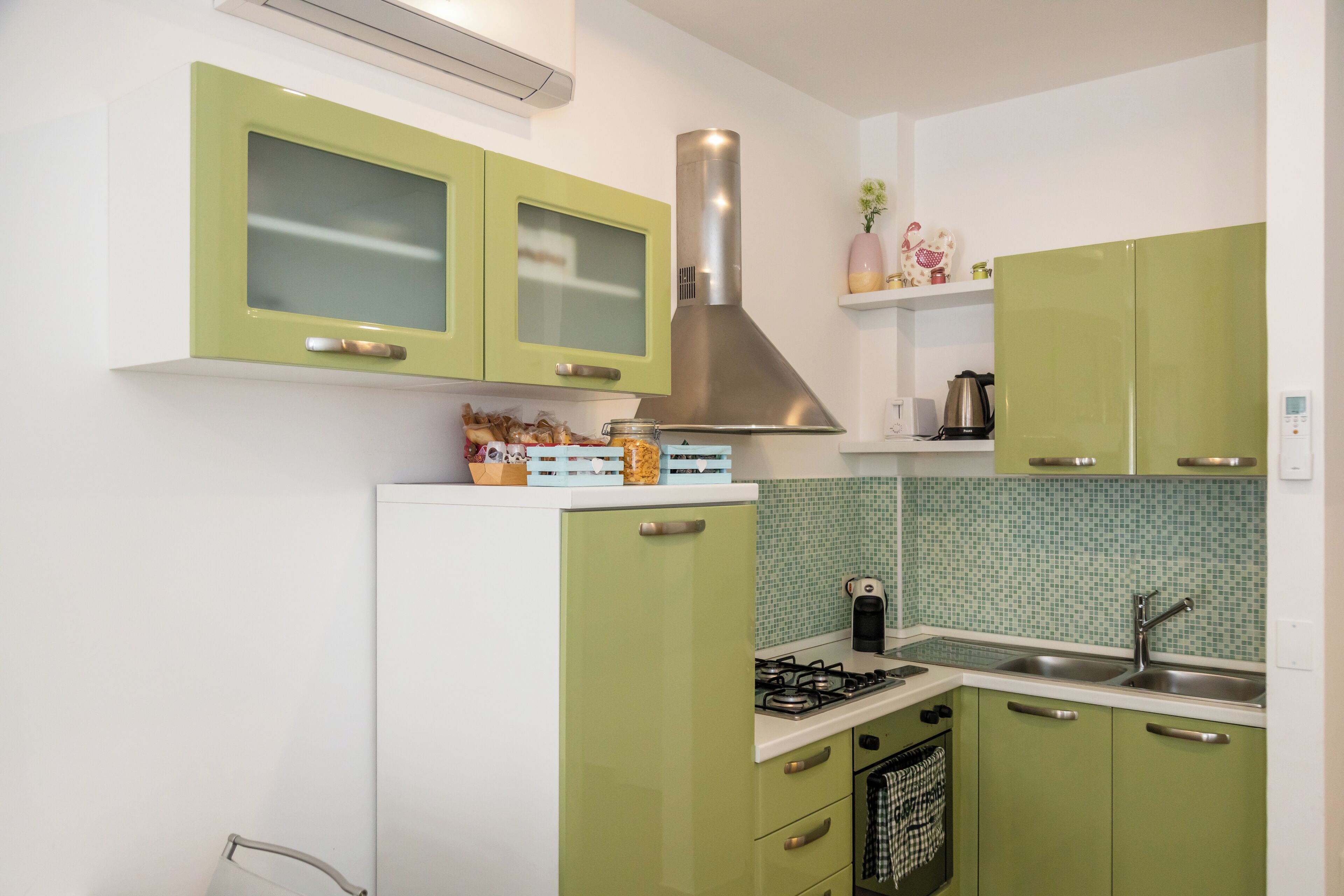 Una cucina con mobili verdi, una cappa in acciaio inossidabile e uno schienale piastrellato.