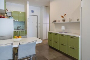 Eine moderne Küche mit grünen Schränken, einer weißen Arbeitsplatte und einem Essbereich mit weißem Tisch und Stühlen.