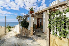 A coastal property with a stone staircase leading to a wooden door, surrounded by greenery and a view of the sea.