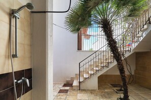 A staircase with a palm tree, a shower, and a window with a view of a building.