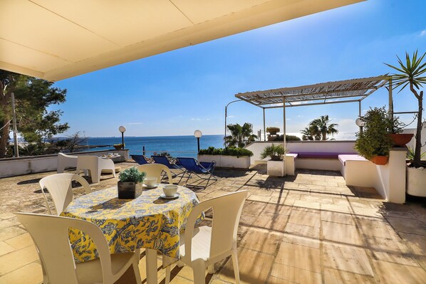 Une terrasse avec une table et des chaises, une pergola et une vue sur la mer.