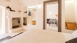 Un dormitorio con cama, cómoda, espejo, perchero y puerta que da a un comedor.