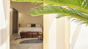 Een smalle gang die leidt naar een slaapkamer met een bed, een dressoir en een klein vloerkleed.