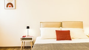 Habitación de hotel ordenada con cama, almohadas, mesita de noche, lámpara y un cuadro en la pared.
