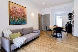 Ein modernes Wohnzimmer mit einem grauen Sofa, einem Esstisch mit Stühlen und einem großen Gemälde an der Wand.