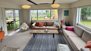 Uma sala de estar moderna com um sofá bege, uma mesa de centro de madeira e uma grande janela com vista para um jardim.