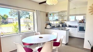 Cozinha moderna com armários brancos, uma ilha central e uma área de jantar com mesa e cadeiras redondas.