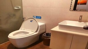 Une salle de bain comprenant des toilettes, une poubelle, un lavabo et un espace douche.