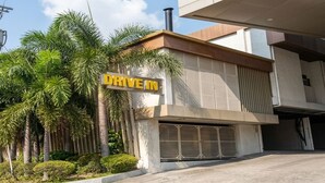 Un bâtiment moderne avec une enseigne « Drive In », entouré de palmiers et doté d’un espace de stationnement.