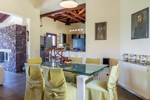 Un coin repas avec une table et des chaises en verre, un mur en pierre et une cuisine en arrière-plan.