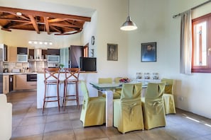 Una cocina moderna con vigas de madera, un comedor con sillas amarillas y un amplio ventanal con cortinas.