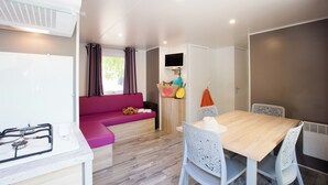 Un espace de vie compact comprenant un coin cuisine, un coin repas avec une table et des chaises, un canapé et une petite fenêtre avec des rideaux.