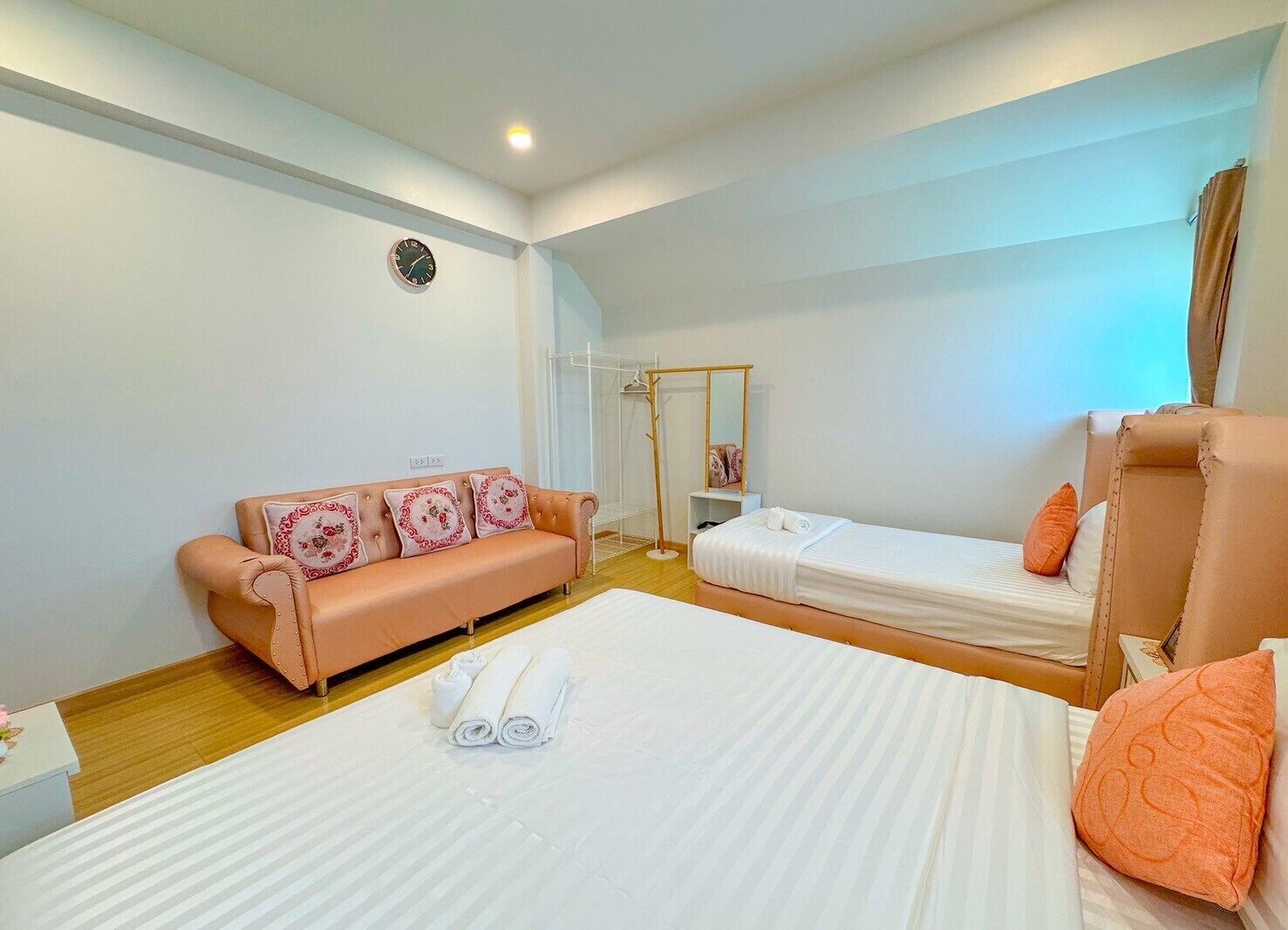 A hotel room with a sofa, two single beds, a mirror, and a clock on the wall.
