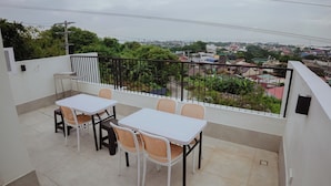 A balcony with a white table and wicker chairs, offering a view of a cityscape with buildings and greenery. - Villa Verde: Relax, Unwind & Stay in Spacious Comfort (Muntinlupa)