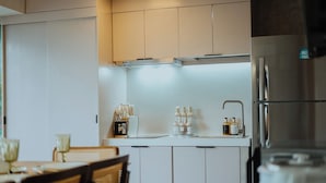 A modern kitchen with white cabinets, a built-in oven, and a refrigerator. There are kitchen utensils and bottles on the counter. - Villa Verde: Relax, Unwind & Stay in Spacious Comfort (Muntinlupa)
