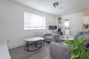 Ein modernes Wohnzimmer mit einer Couch, zwei kleinen Tischen, einer Heizung und einem Fenster mit Jalousien.