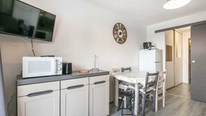 A compact kitchen with a microwave, toaster, and a coffee machine on the counter. There is a dining table with chairs and a wall-mounted clock. - Charming studio apartment, sleeps 6-7, mountain view (Chamrousse)